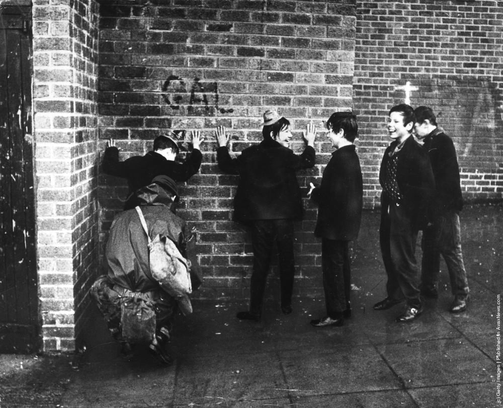 Schoolboys giggling while a soldier searches them in a street in the Ardoyne area of Belfast, 7th December 1971.