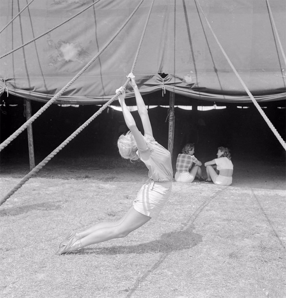 An acrobat practicing with a tent rope while two girls are sitting nearby during a rehearsal for the Ringling Bros. and Barnum & Bailey Circus in Sarasota, FL in 1949.