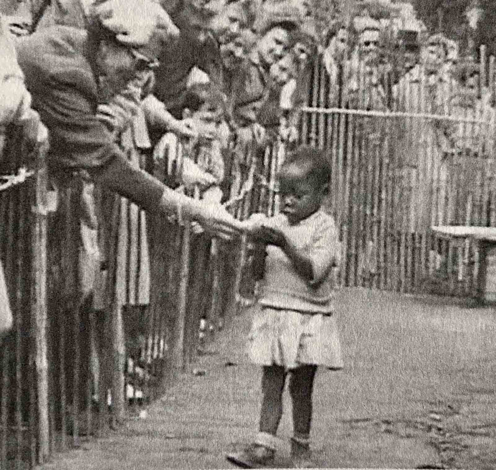An African girl at the 1958 Expo in Brussels, Belgium that featured a ‘Congo Village’ with visitors watching her from behind wooden fences.
