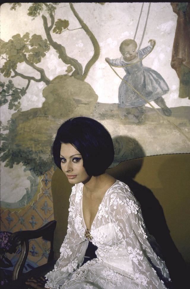 Sophia Loren wearing a white dress, sitting in front of a painting in her villa.