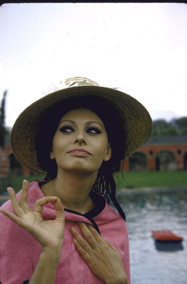 Sophia Loren wearing a pink wrap and straw hat out by the pool at the villa.