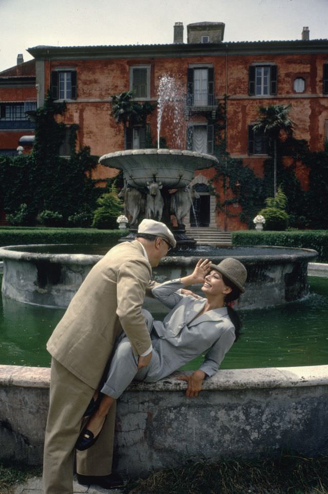 Sophia Loren and Carlo Ponti posing in front of a large fountain at their villa.