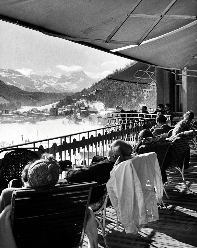 Guests at fashionable winter resort napping and sunbathing on hotel terrace after lunch.