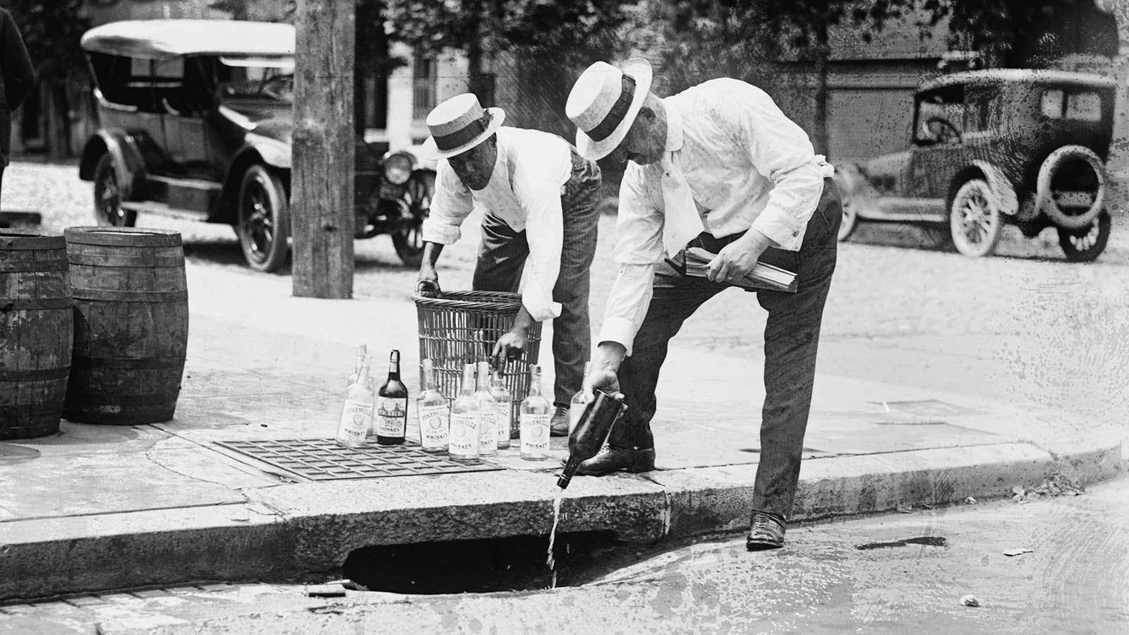 Two men pour alcohol down a drain during prohibition in the United States, c. 1920.