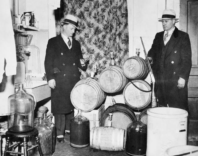 Police officers look over distilling equipment and guns confiscated during a Prohibition raid, Chicago, ca.1920s.