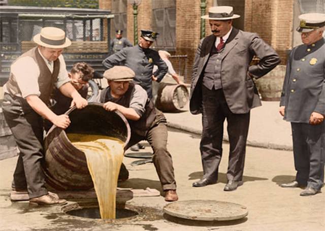 New York City Deputy Police Commissioner John A. Leach (right) watches as agents pour liquor into a sewer following a raid during the height of Prohibition.