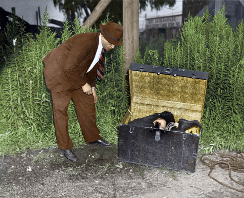 Newspaper photographer Arthur Fellig, better known as Weegee, examines a body stuffed into a trunk and deposited on a patch of waste ground in New York, 1945.