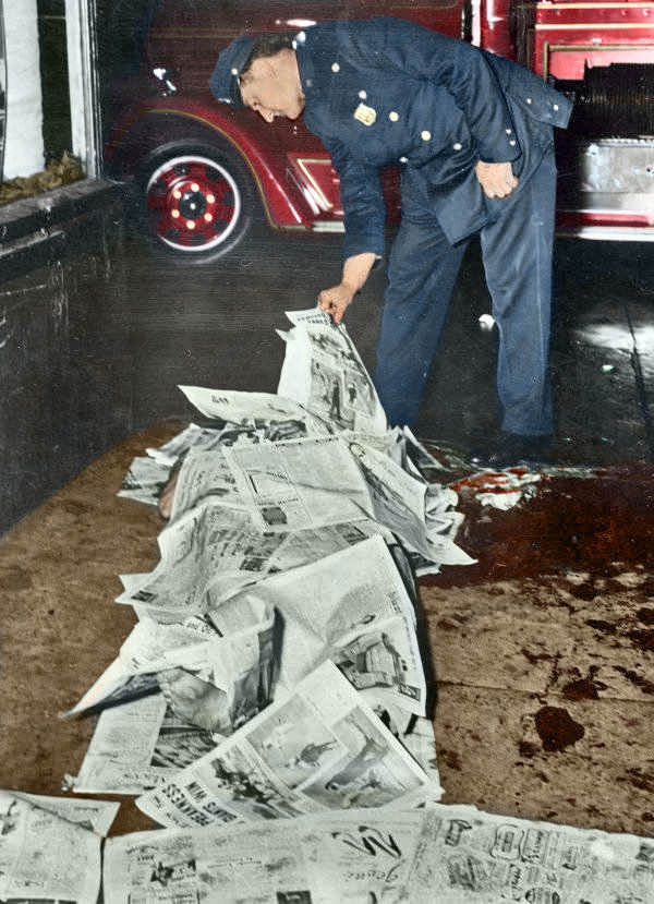 A New York police officer takes a peek at a dead body covered with newspapers, 1943.