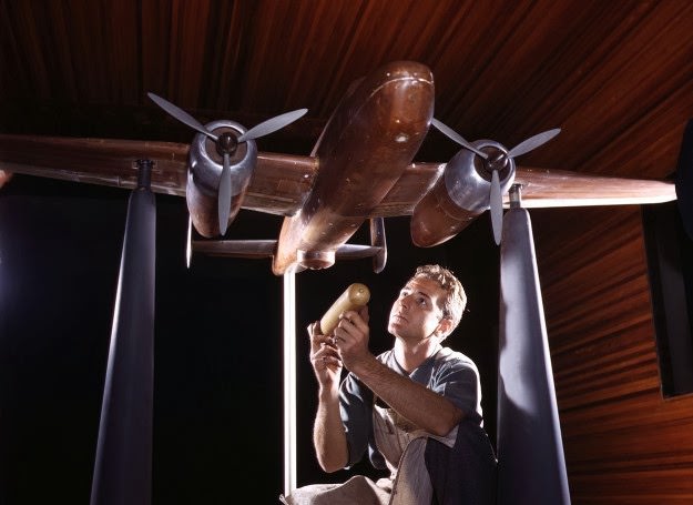 An experimental scale model of the B-25 plane is prepared for wind tunnel tests in the plant of the North American Aviation, Inc., Inglewood, California. The model maker holds an exact miniature reproduction of the type of bomb the plane will carry. October, 1942