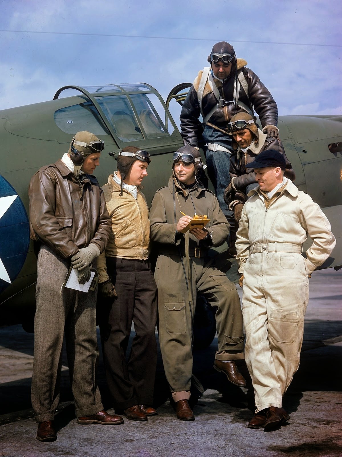 Curtiss Wright's chief test pilot H. Lloyd Child (center) writes on a clipboard as he stands with other pilots on a tarmac near the companies manufacturing plant, Buffalo, New York, 1941.
