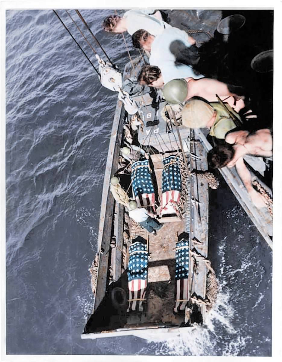 Deceased US soldiers are wrapped in their national flag and carefully lowered down onto a ship by comrades ready for burial.