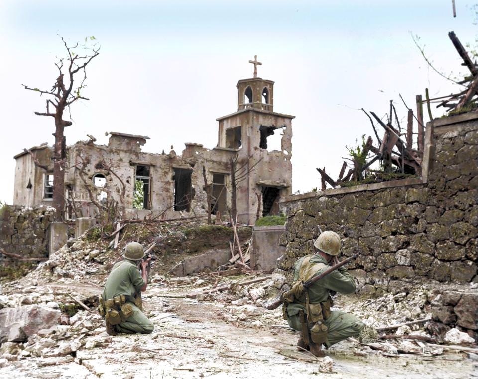 While a patrol moves in from the rear, two United States Marines cover a Japanese sniper hiding in a church, below Shuri Castle on Okinawa, 1945.