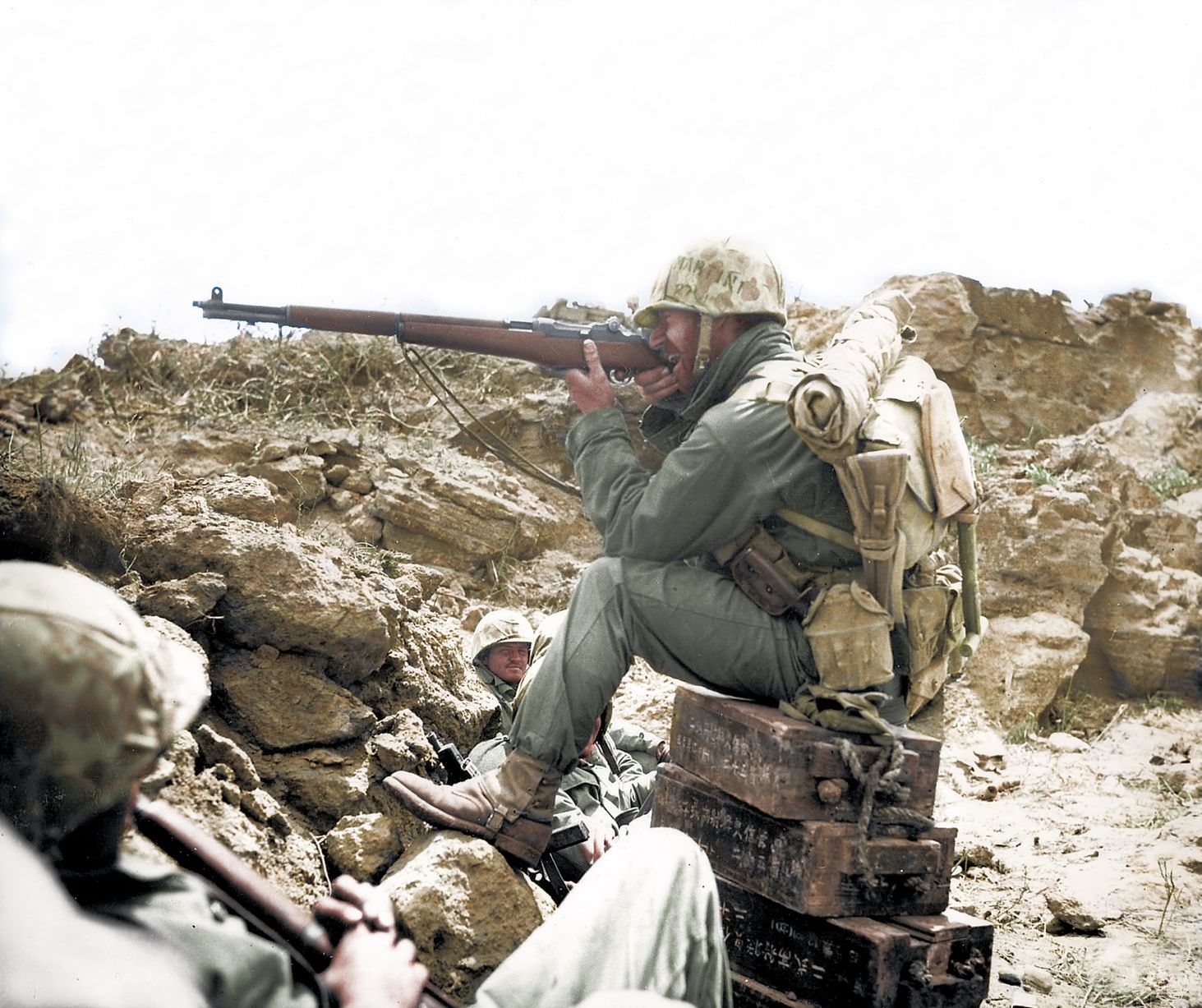 A US marine takes aim while sitting on Japanese ammunition boxes.