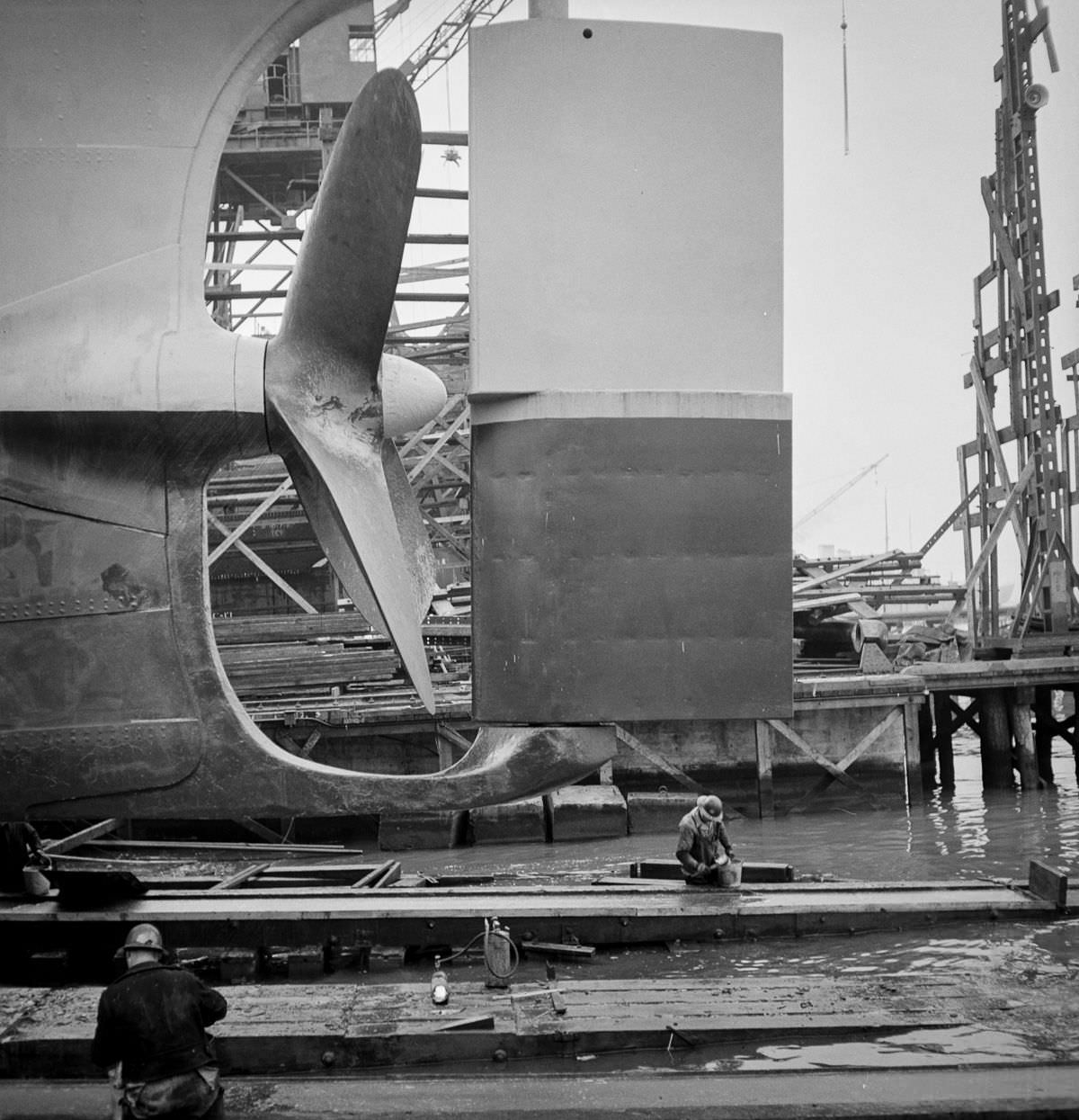 Workers grease the outboard end of a way before a launching