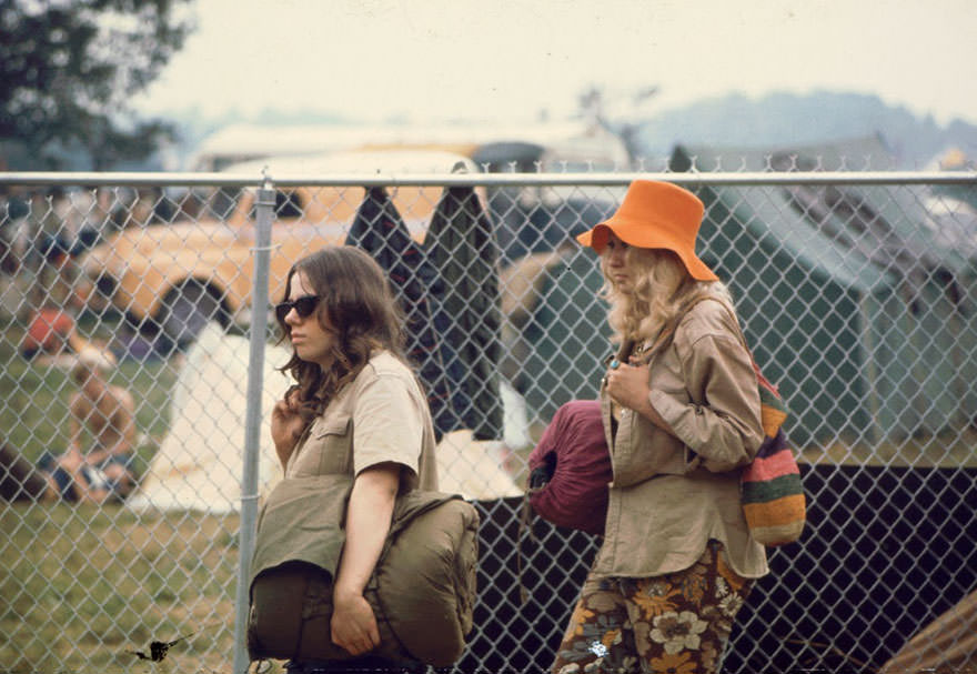 Two Young Women Walking Along The Fence With Sleeping Bags At The Woodstock Music Festival