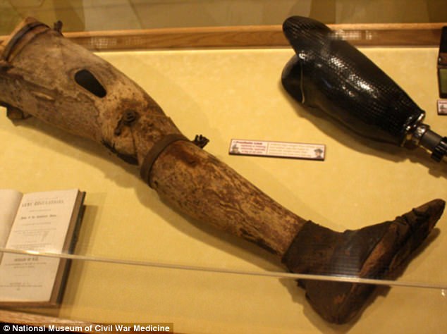 This prosthetic leg made of wood is a full left leg, articulated at the knee, with a leather shoe covering the foot. It still retains some of the original flesh-colored paint.