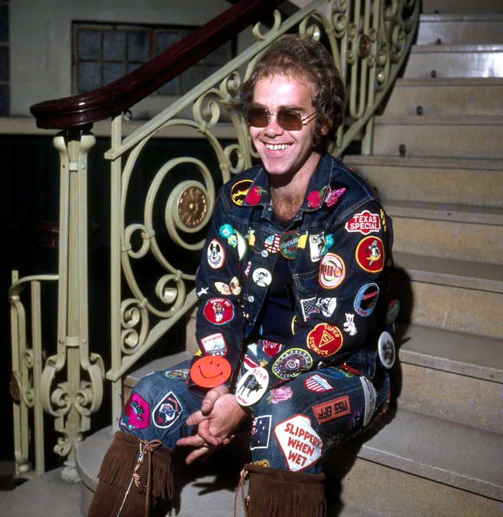 Elton John wearing double denim covered in embroidered patches.