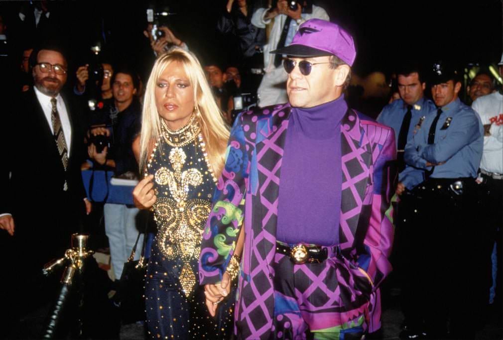 Elton John in a purple silk Versace suit and matching Nike cap at Planet Hollywood’s launch party, 1991