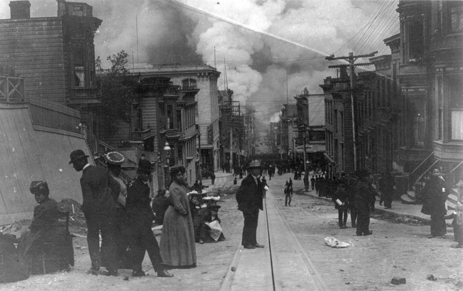 African American families on street during the San Francisco Fire of 1906, with clouds of smoke billowing at bottom of hill in background.