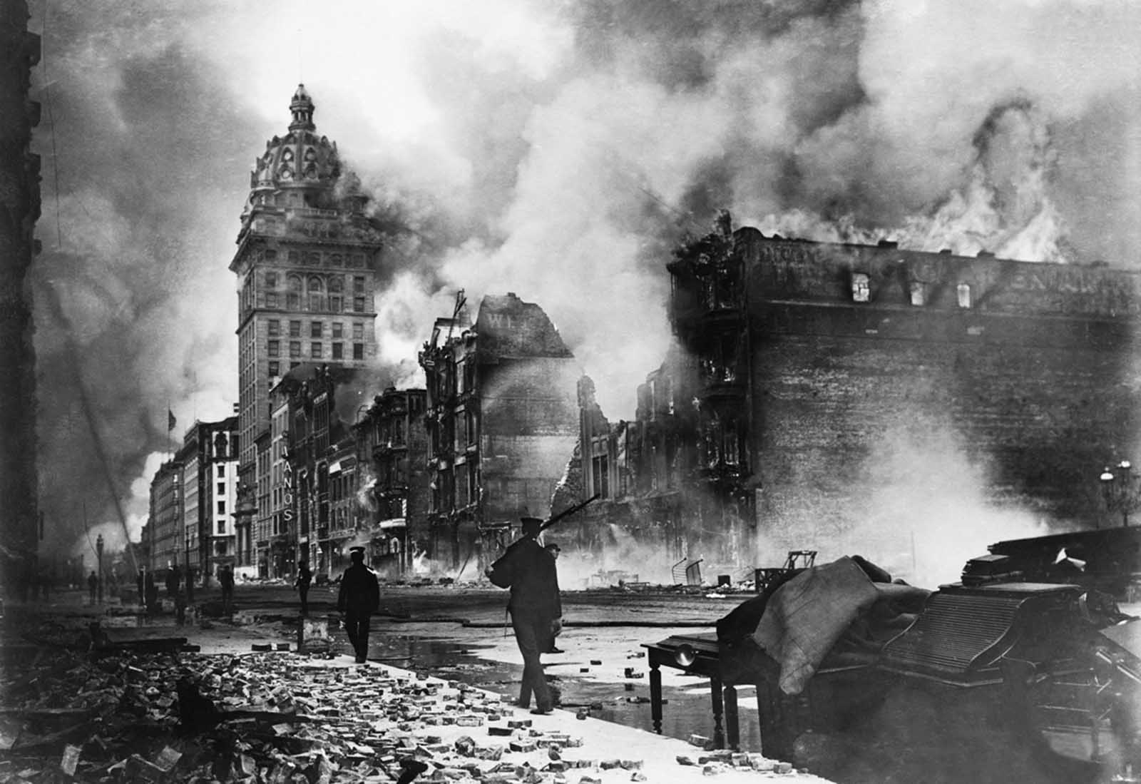 Troops walk east along Market Street after the devastating earthquake of 1906. The Call building burns in the distance