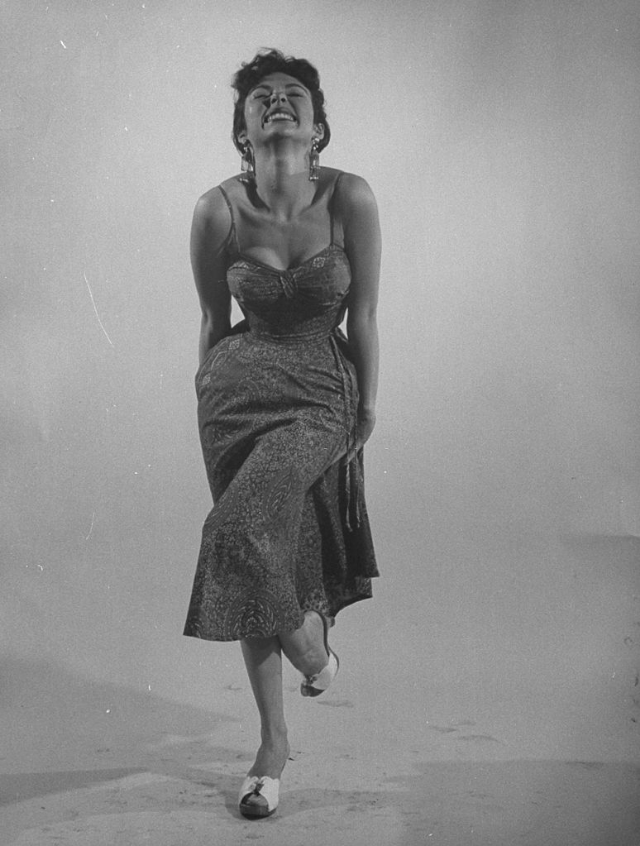 Rita Moreno imitating the sexy-wild actress by raising one leg in her tight and sexy semi-revealing dress, 1954.