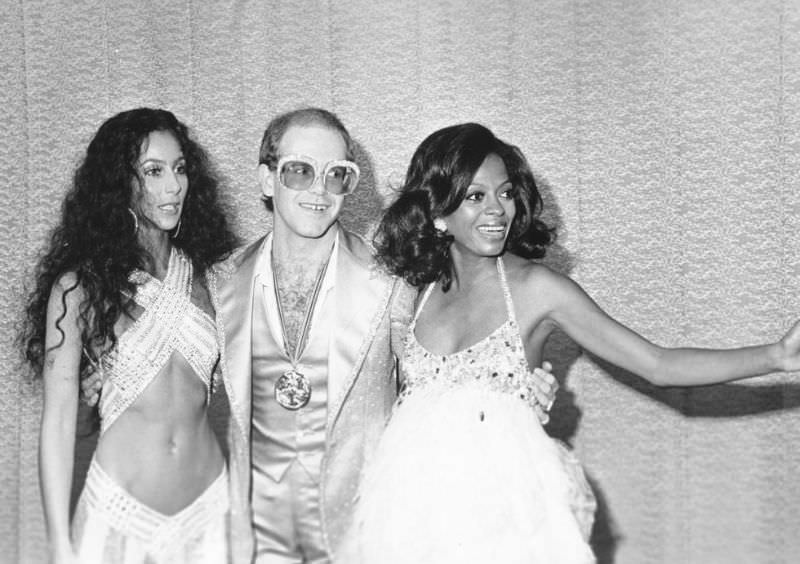 Cher, Elton John, and Diana Ross pose together while backstage at the first Rock Music Awards in Los Angeles in 1975