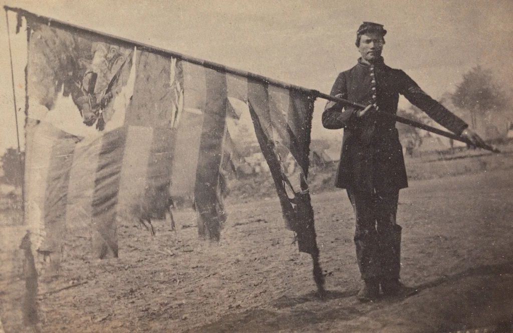 Portrait of Union color bearer Alex Rogers of the 83rd Pennsylvania Volunteer Infantry Regiment posing with a battle-shredded battle flag after the Battle of Gettysburg, 1863.