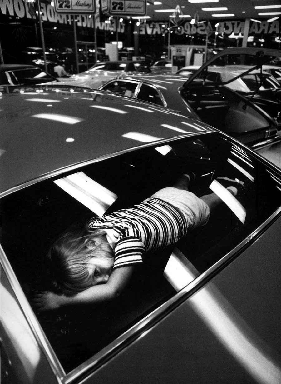 A young girl tries out the "best" seat in a car while her parents shop for one. Atlanta, Georgia, 1971