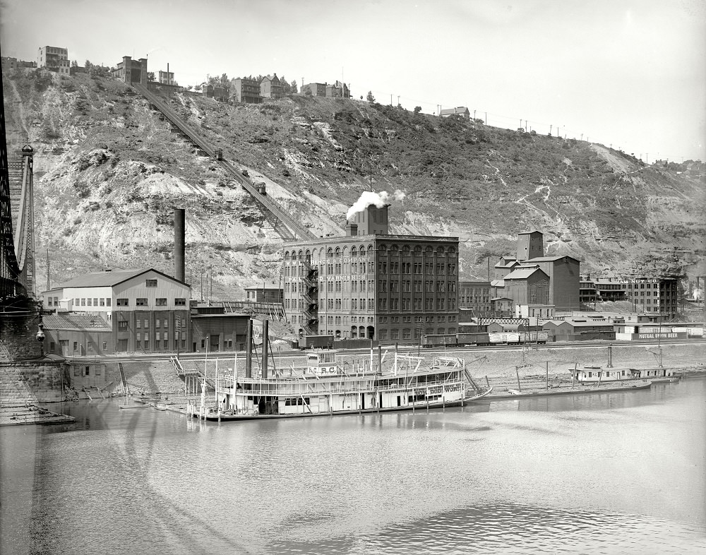 Duquesne Incline Railway. Mount Washington and the Ohio River feature in this view, which includes the Point Bridge, a paint and varnish factory, a riverboat and the Graham Nut Company, Pittsburgh, Pennsylvania, circa 1900-1910