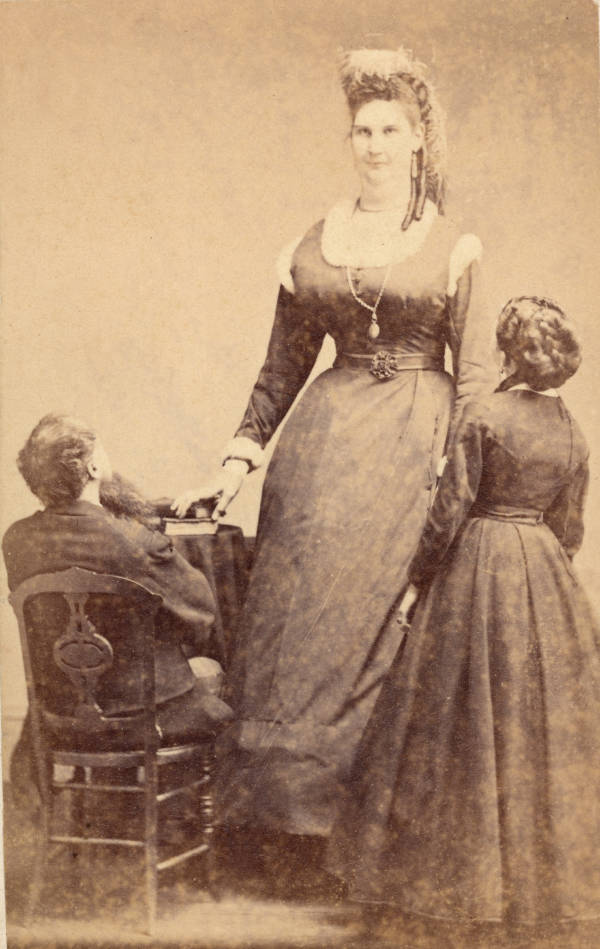 Canadian circus performer Anna Haining Swan Bates poses next to her father Alexander Swan (seated) and her mother Ann Haining Swan, a woman of average height, 1870s