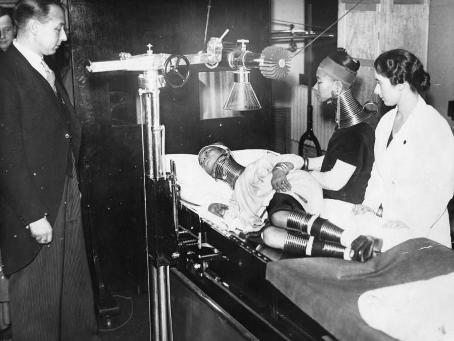 Members of Bertram Mills' "freak" show are examined by doctors. On the examination table is the "Giraffe Necked Woman." 1935