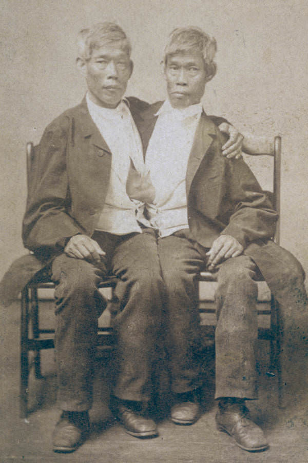 Portrait of American Siamese twins Chang and Eng Bunker sitting on two wooden chairs,, 1865