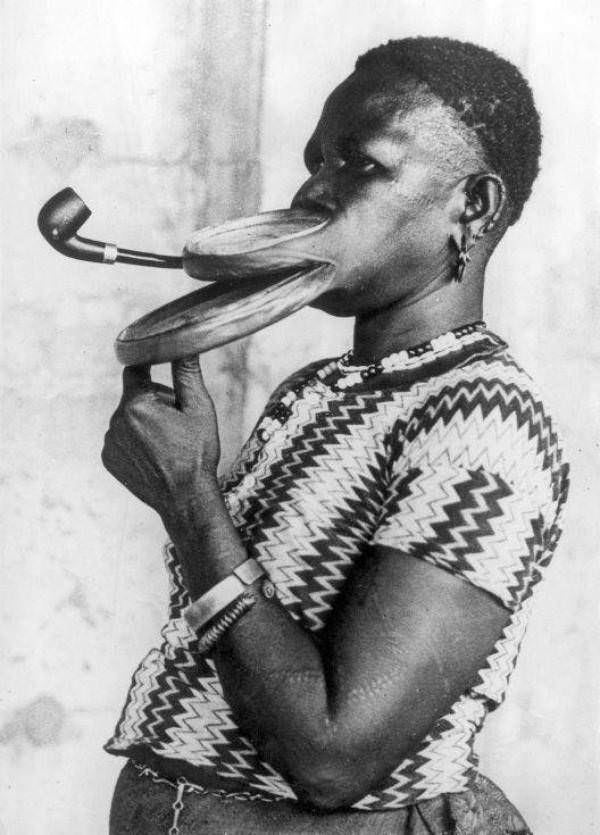 Madam Gustika, who was billed as being from the "Duckbill tribe," is seen here smoking a pipe through the large plates in her lip, 1930