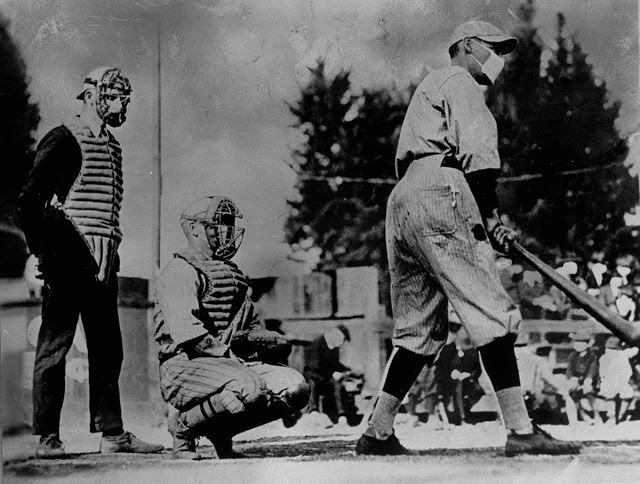Unident baseball players, one batting and one catching, plus an umpire behind the plate, wear flu masks, 1918.