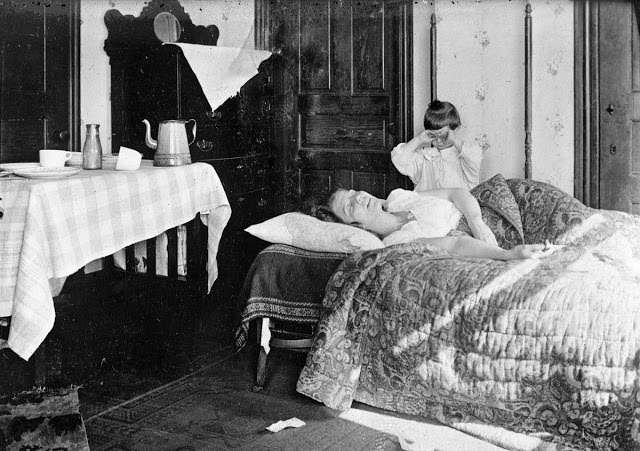 A girl stands next to her sister, who is lying in bed, in November of 1918. The young girl became so worried that she telephoned the Red Cross Home Service, which came to help the woman fight the influenza virus.