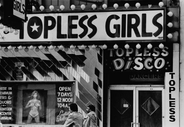 Two men walking past the entrance to a topless disco, New York City, circa 1980.