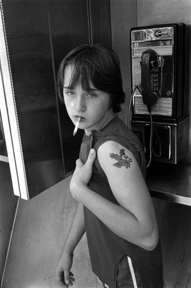 A teenage hustler smoking in a telephone booth.