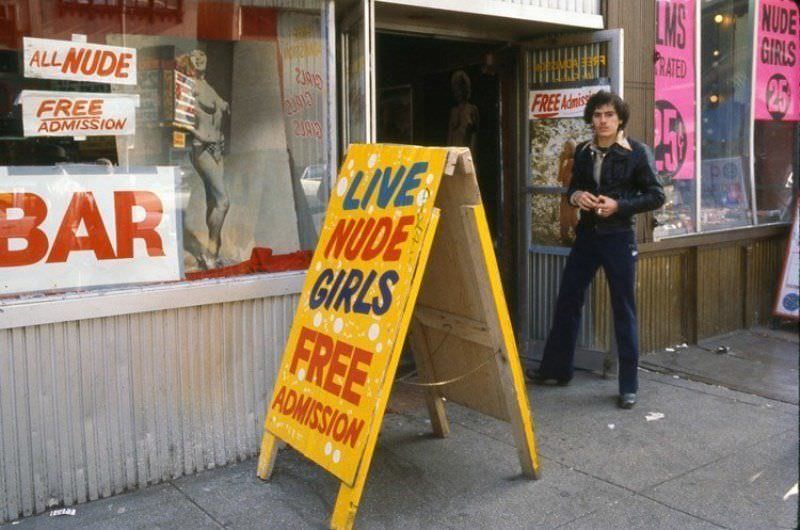 A man stands outside of a strip club on 42nd Street in the late 1970s.