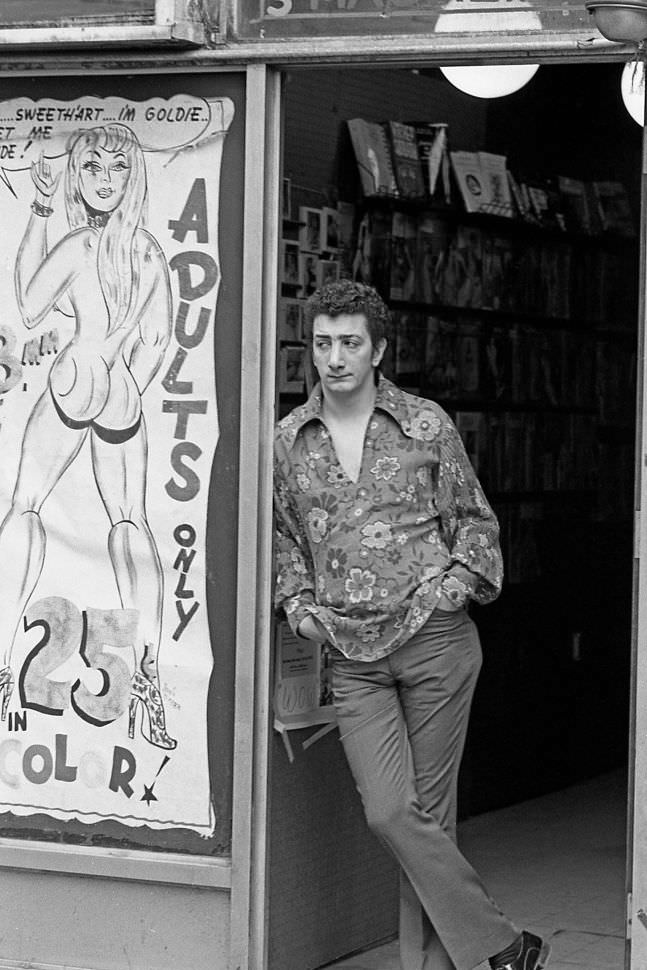 A salesman at a sex shop surveys his storefront as he waits for customers to stroll by. 1970