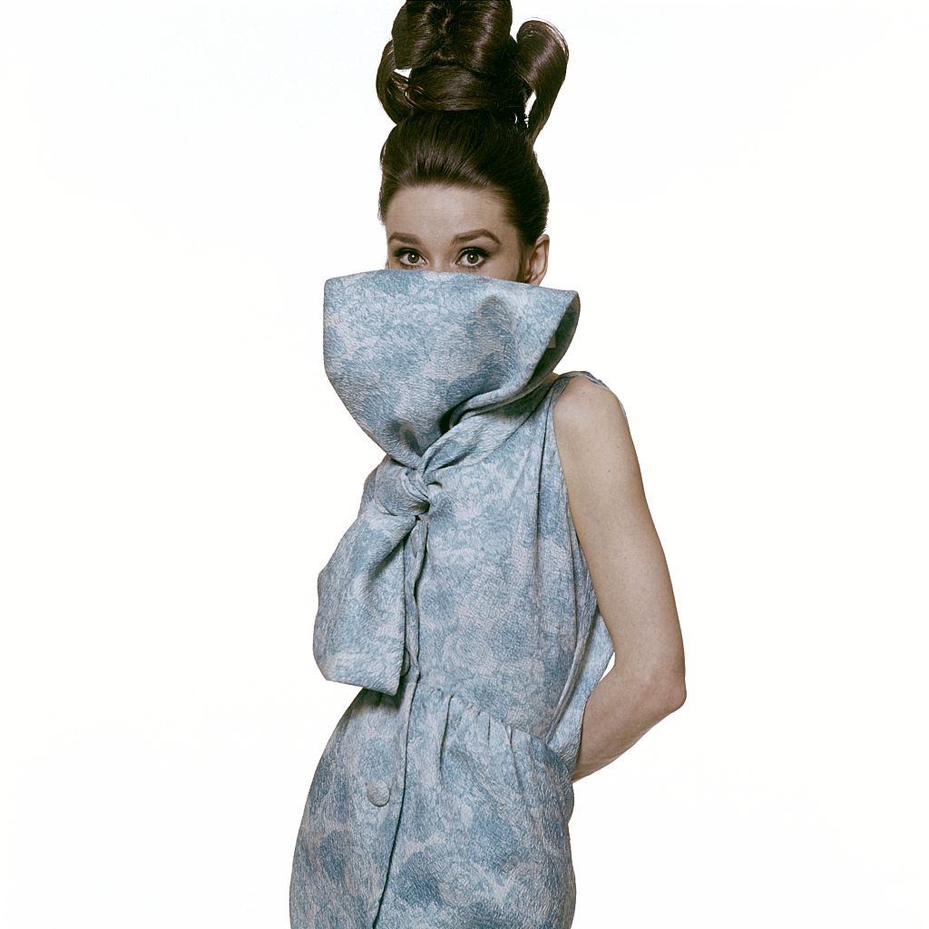 Audrey Hepburn covering portion of face with fabric from her sleeveless dress of silk, Vogue 1963