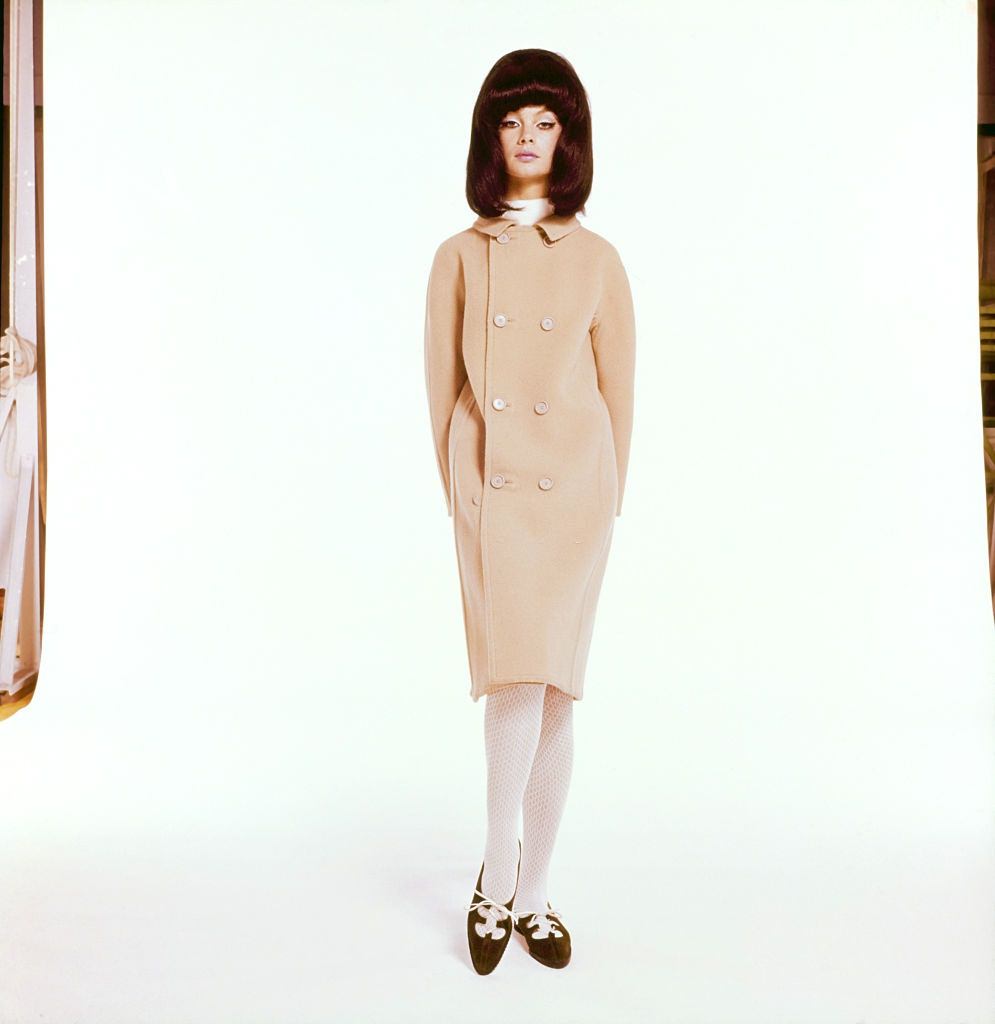 Fashion model wearing double breasted coat in putty beige melton, by Originala, with white textured tights, Vogue 1964