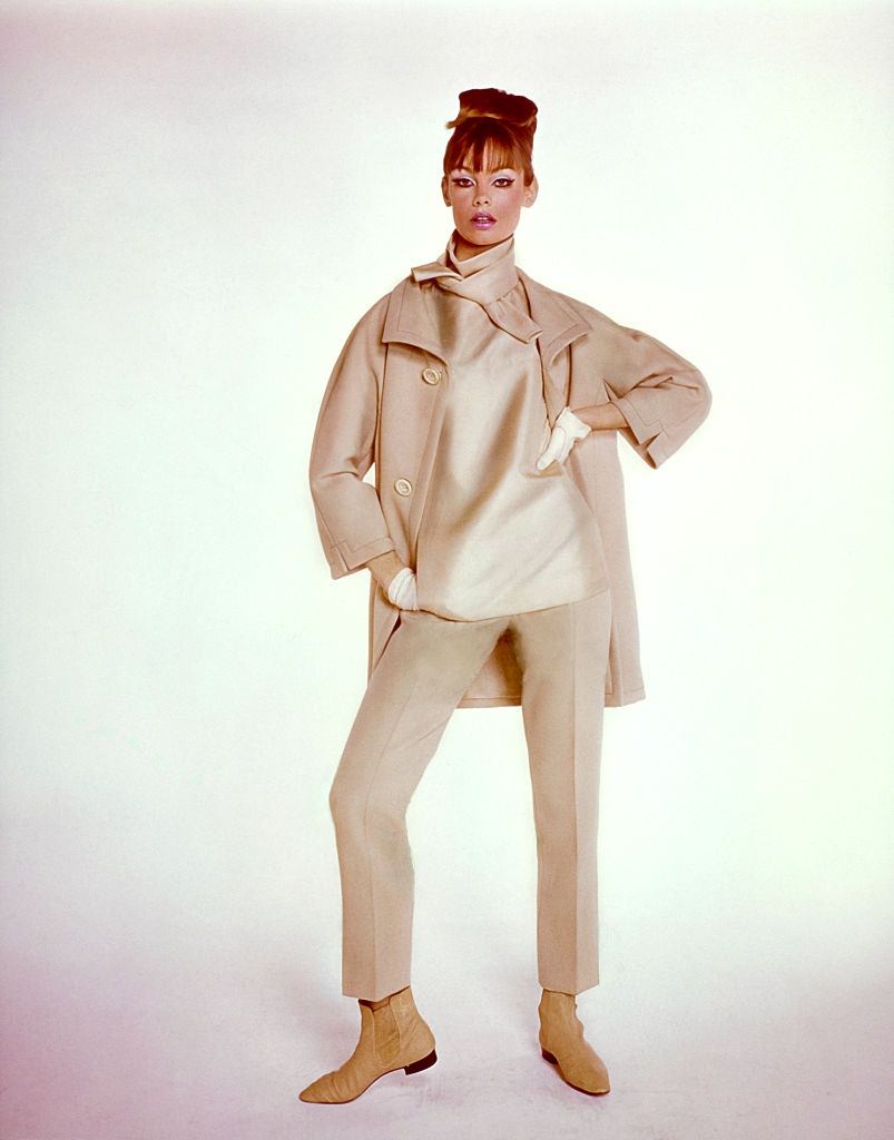 Model Jean Shrimpton wearing trouser ensemble in shades of beige, with coat, trousers, and tie neck top, Vogue 1964