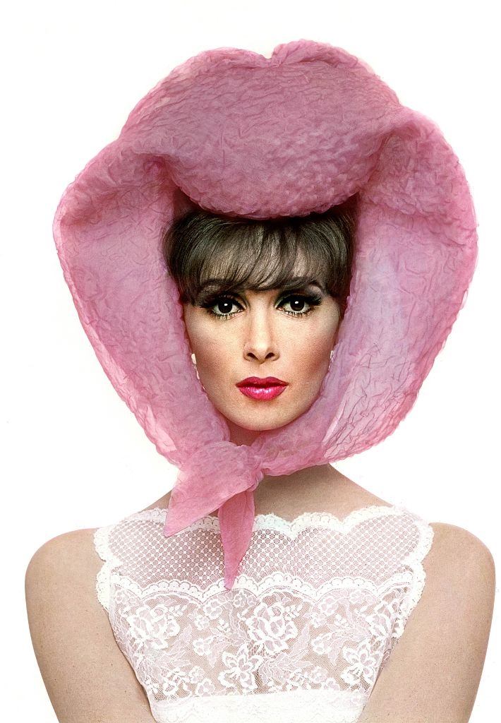 Model Wilhelmina with pink Lilly Dache scarf around head and white lace dress, Vogue 1964