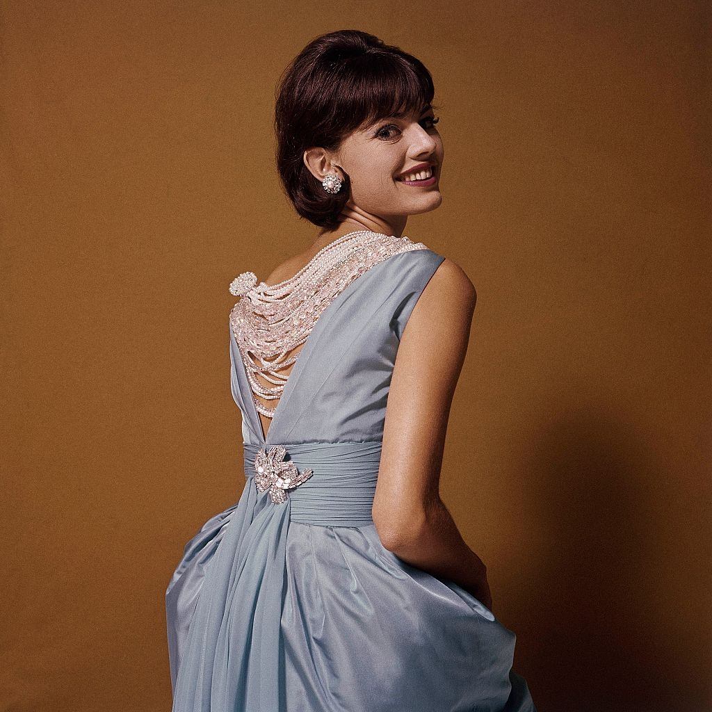 Fashion Model looking over shoulder wearing blue dress which has a V shaped back, Glamour 1960