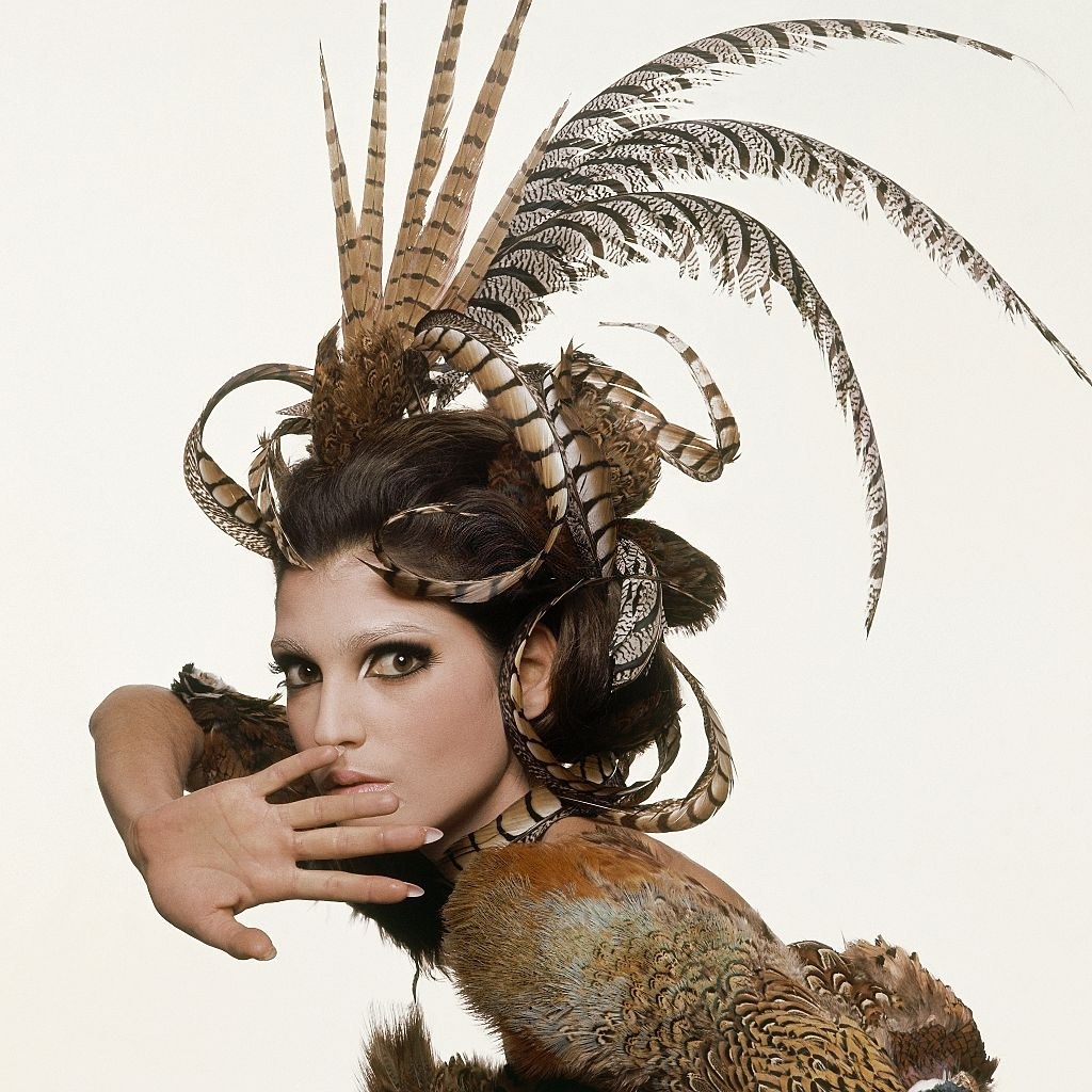 Fashion model from series of beauty shots based on the four seasons, here for autumn 1965, with elaborate feather headdress, covered up eyebrows, and heavy lashes, Vogue 1965
