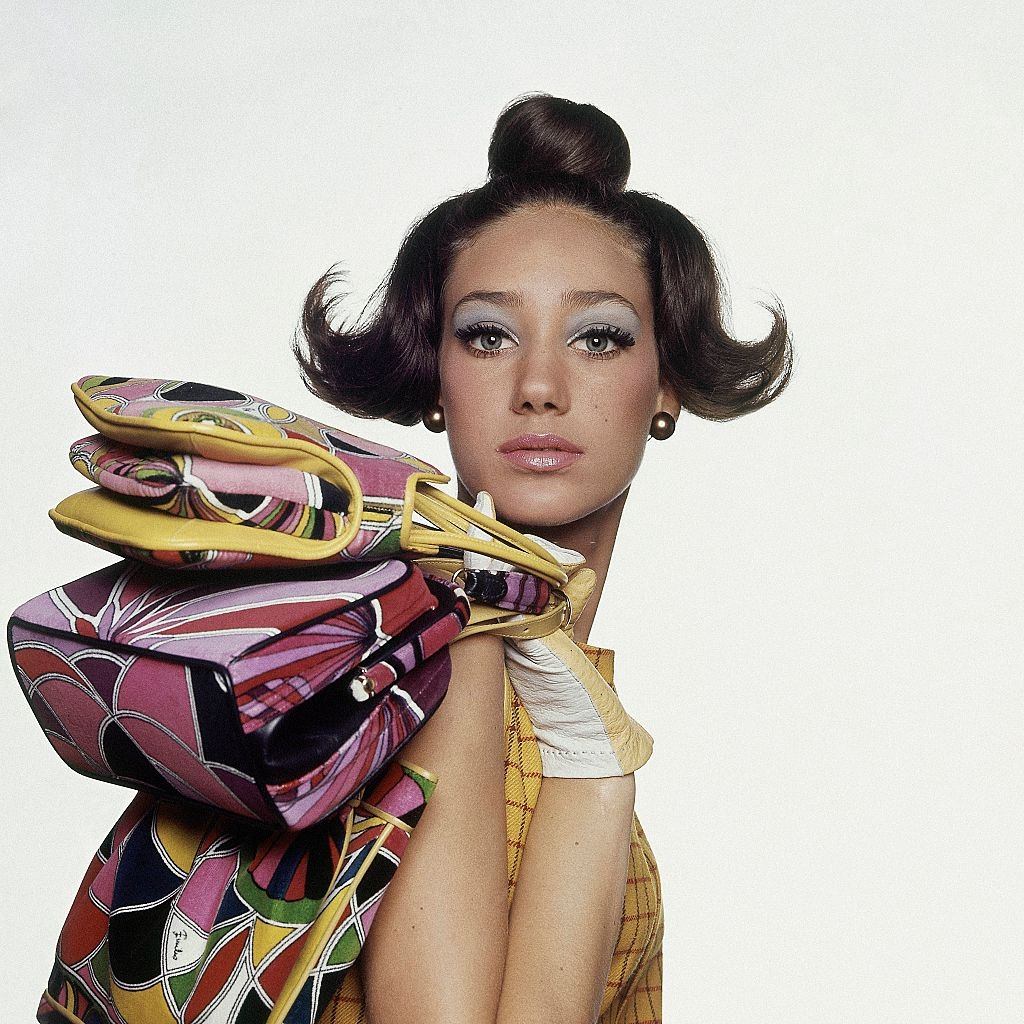 Model, Marisa Berenson, with three Pucci velveteen handbags over her shoulder, in a sleeveless yellow dress, Vogue 1965