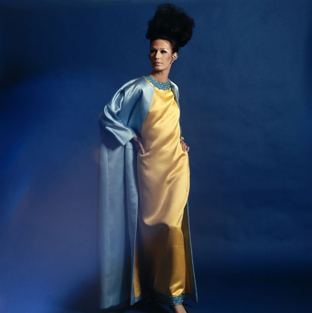 Model wearing a Harold Levine blue satin coat and crystal jeweled yellow full-length dress, Vogue 1965