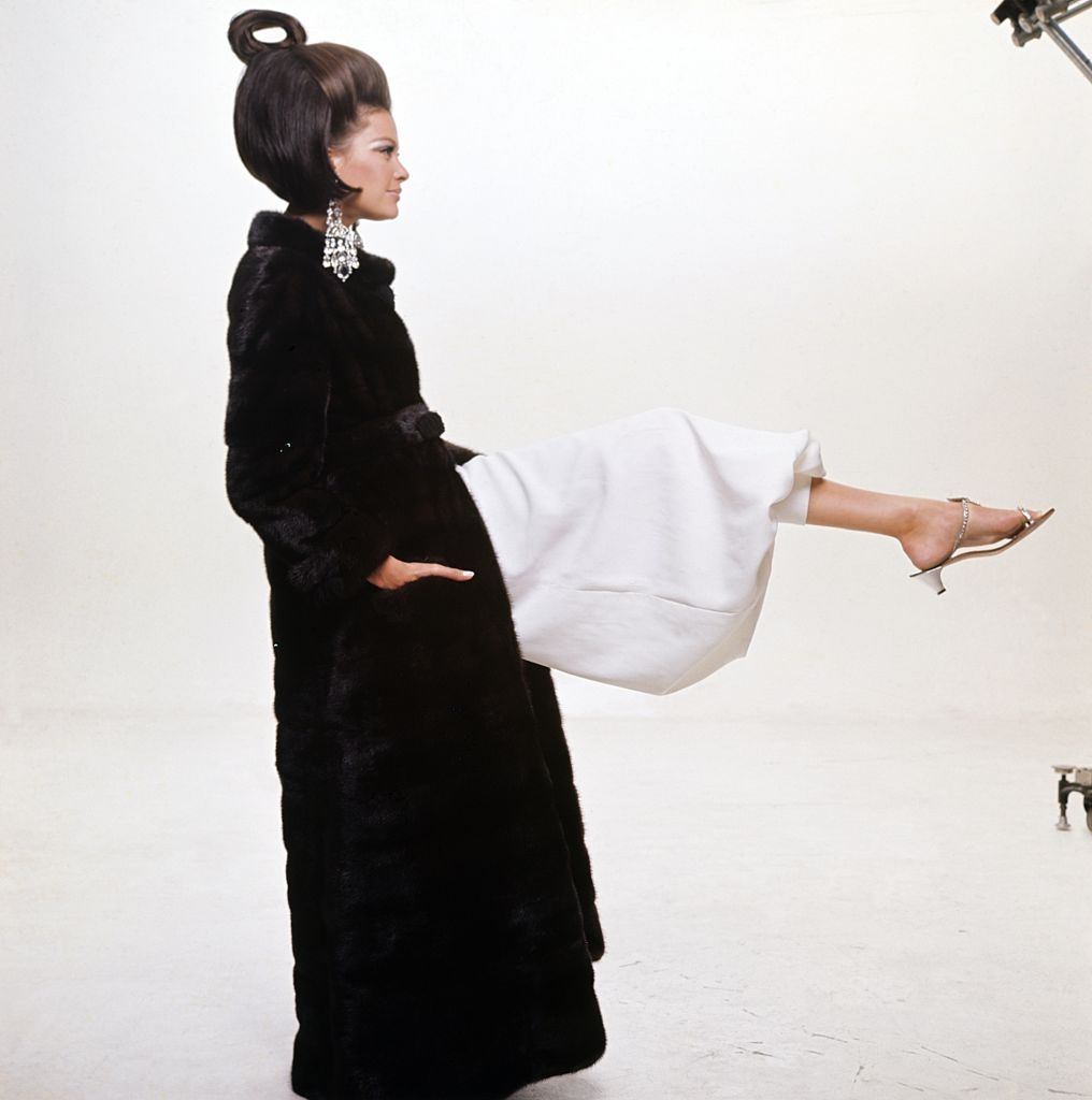 Model wearing full-length mink coat by Maximilian over white evening pyjamas, Vogue 1966