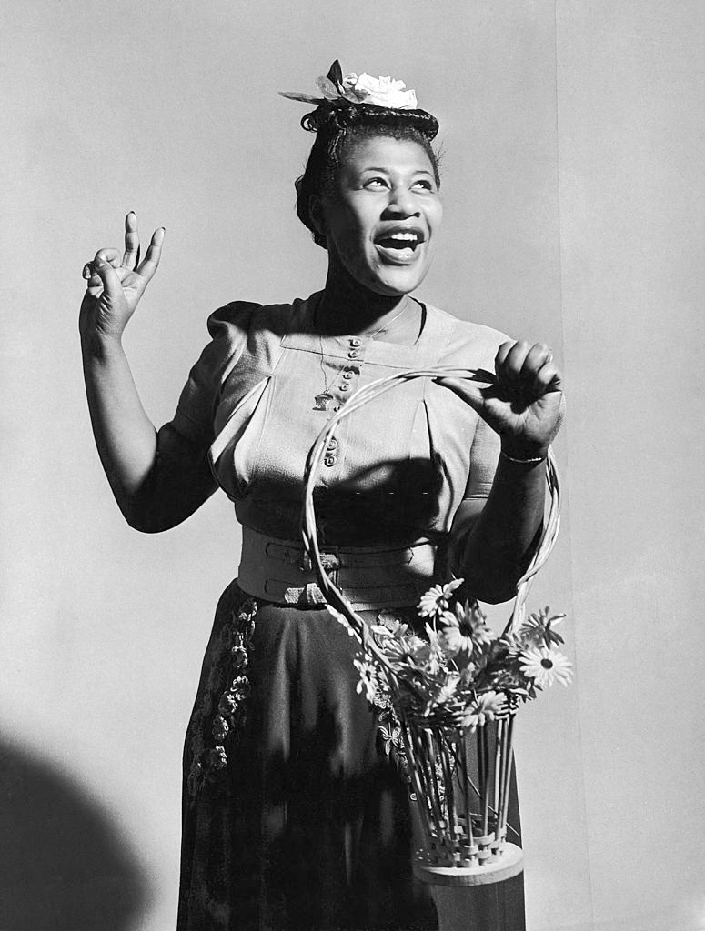 Ella Fitzgerald holding a basket of flowers as she sings A Tisket, a Tasket in front of backdrop, 1946
