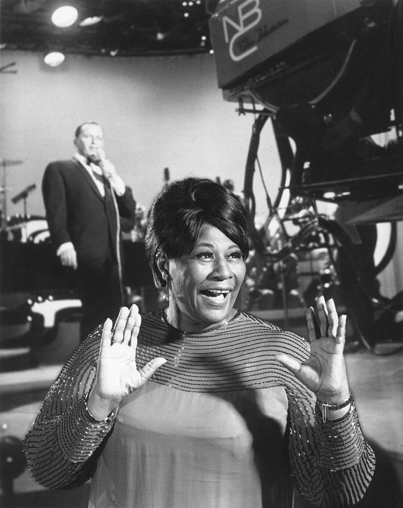 Ella Fitzgerald appears onstage with pop singer Frank Sinatra in the background in circa 1959